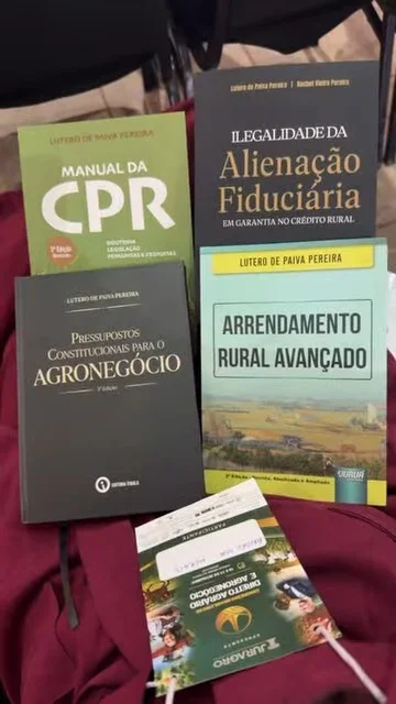 Quatro livros de Direito Agrário de Lutero de Paiva Pereira, entre eles o Manual da CPR e Arrendamento Rural Avançado, sobre o conjunto vinho, com o crachá do congresso da Juragro.